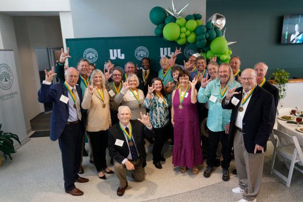 A group of people posing for photo in front of a JU panel ornated with green ballons.